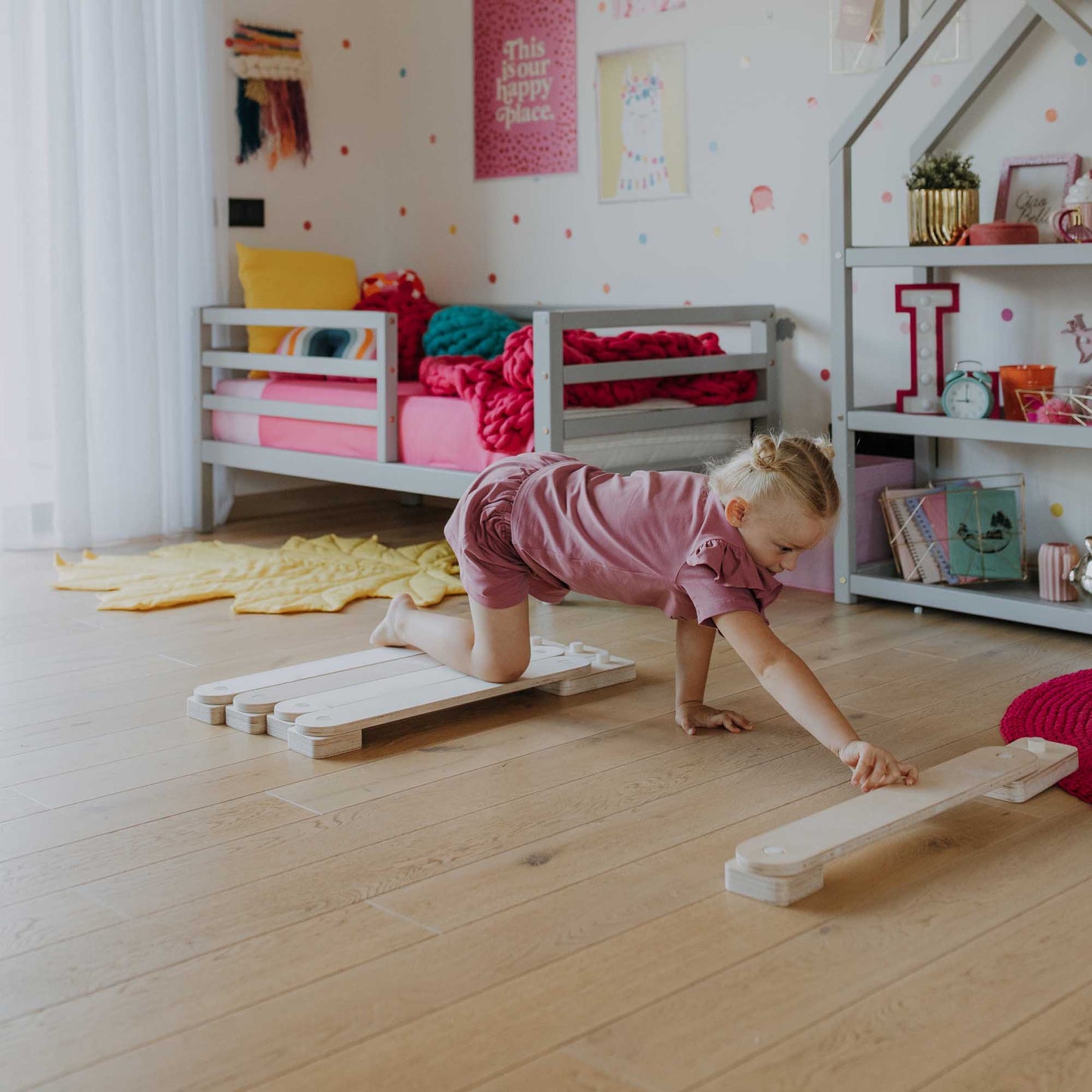 A little girl playing with the Sweet Home From Wood balance beam set as an indoor climber in her room.