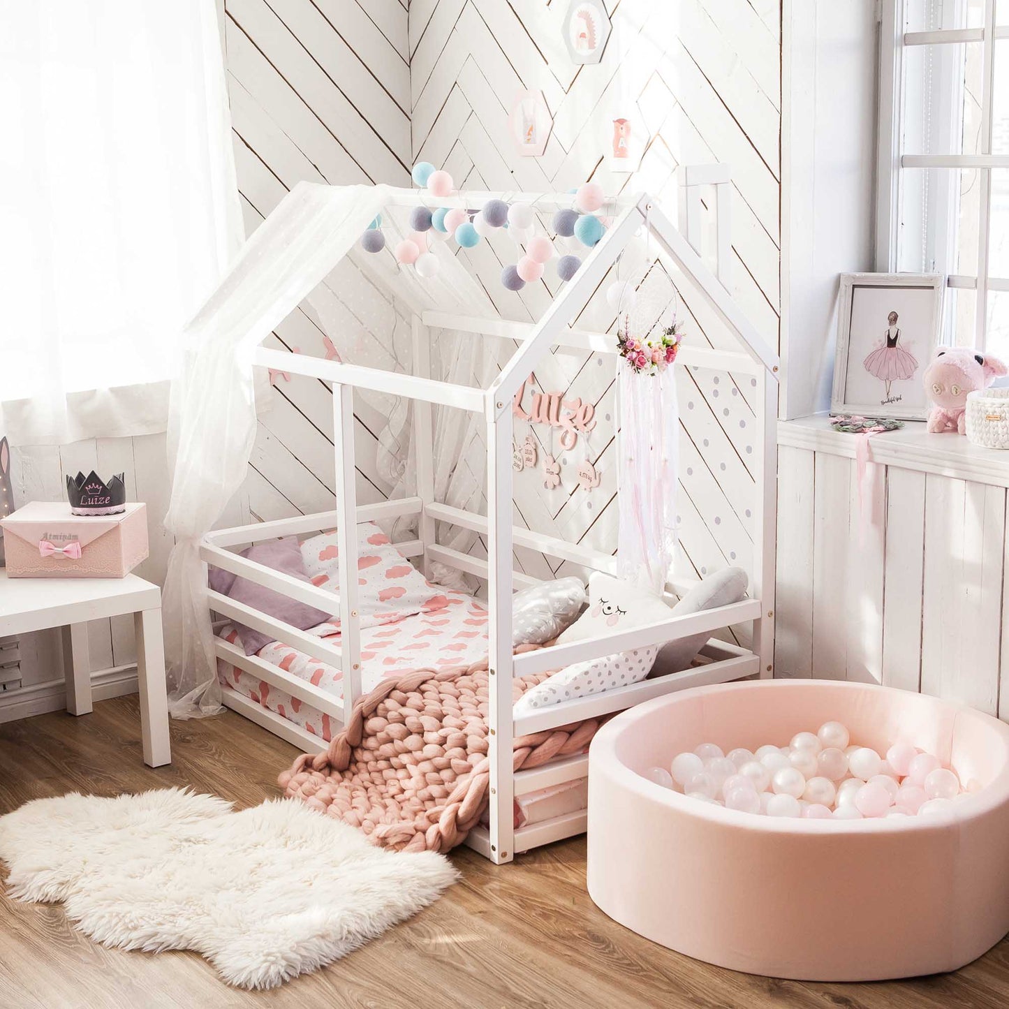 A girl's room with a pink bed and a floor level house bed with a horizontal fence.