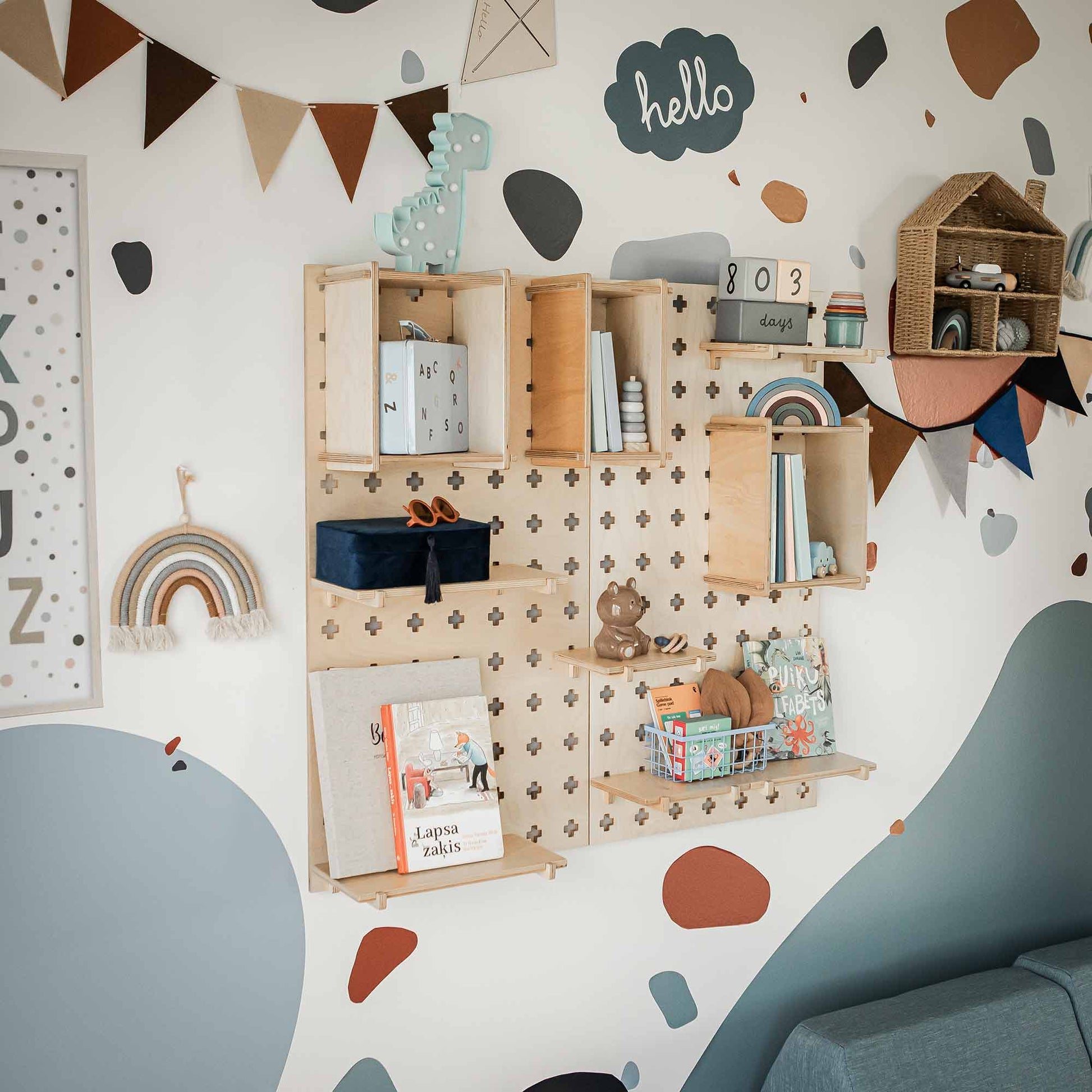 The Large Pegboard Display Stand with books, toys, and decorative items in a room adorned with pastel-colored wall decals and a banner offers a versatile storage solution perfect for decluttering any space.