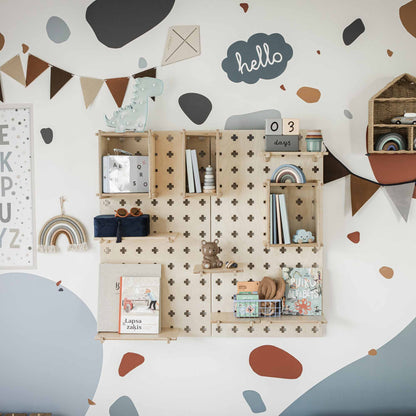 A child's room wall with decorative wooden shelves holding books, toys, and ornaments. The wall is adorned with dotted patterns, bunting, and a sign that reads "hello." A "03 days" countdown is displayed. The Large Pegboard Display Stand provides a clever storage solution for easy decluttering.