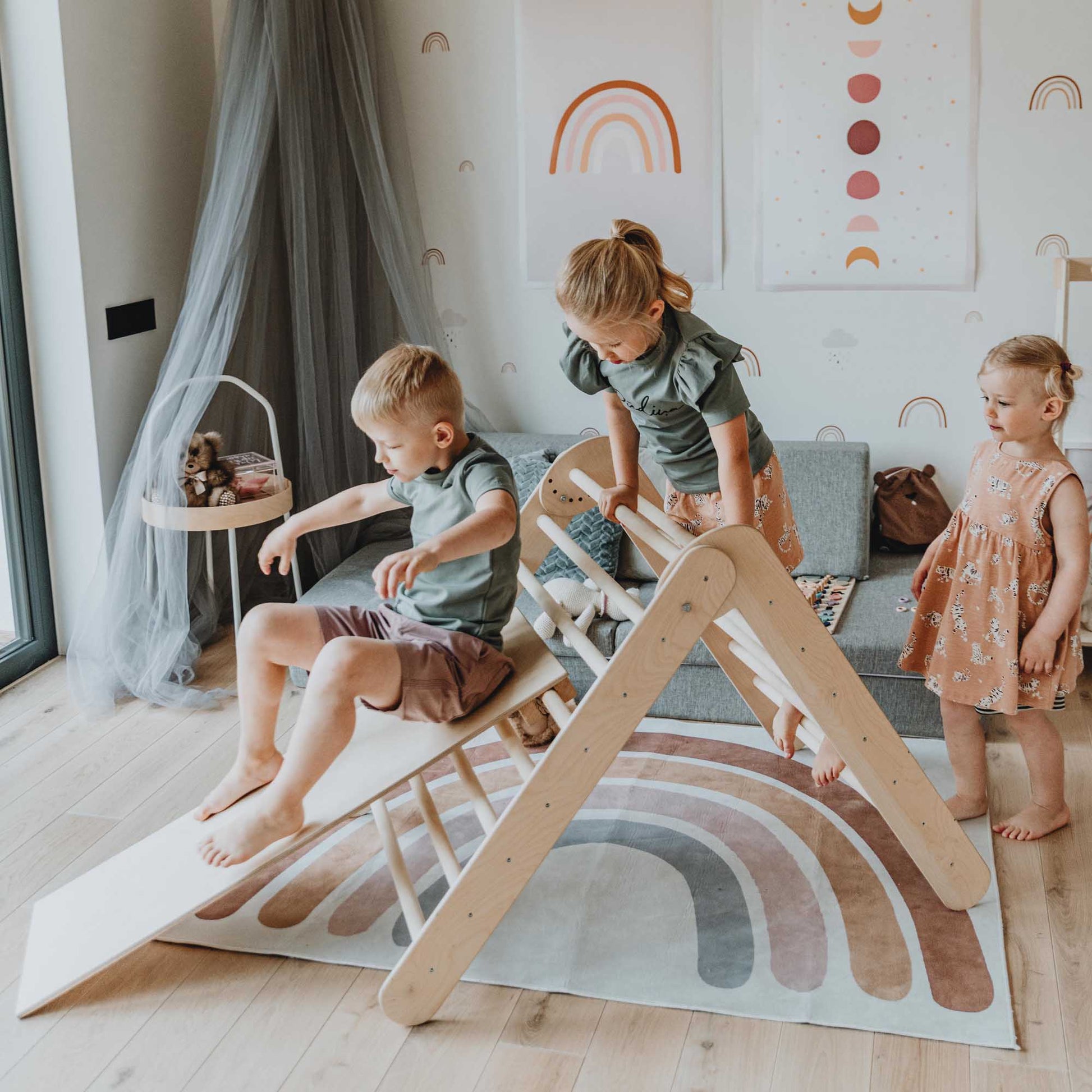 Three children practicing their motor skills on a Foldable climbing triangle with 2 slope levels in a living room.