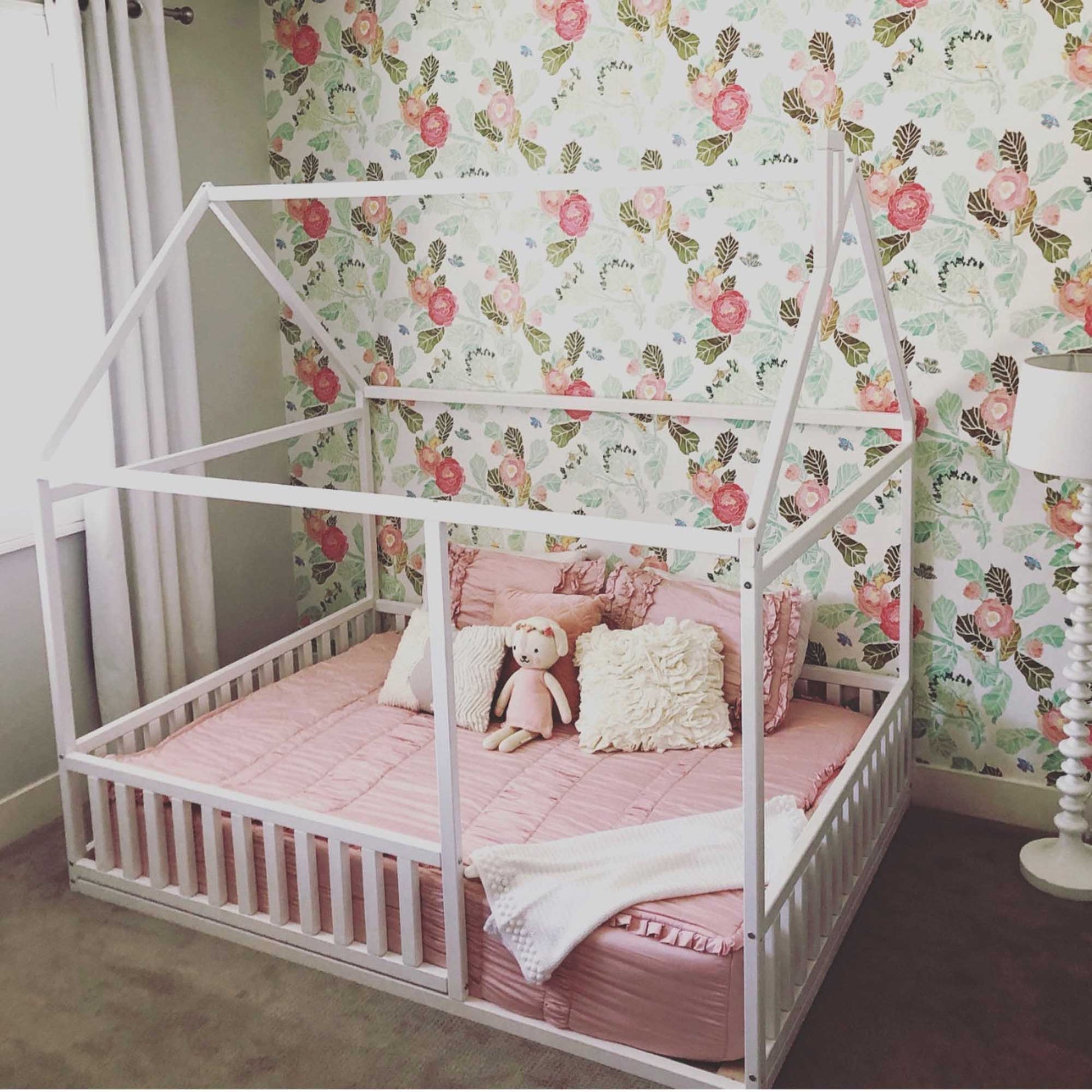 A cozy sleep haven, featuring a Sweet Home From Wood Montessori floor house bed with rails and white bed frame, adorned with pink bedding.
