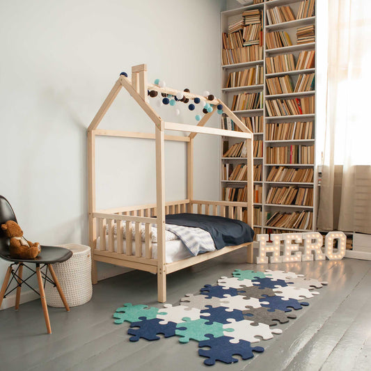 A child's bedroom with a raised house bed on legs with 3-sided rails and wooden bookshelves.