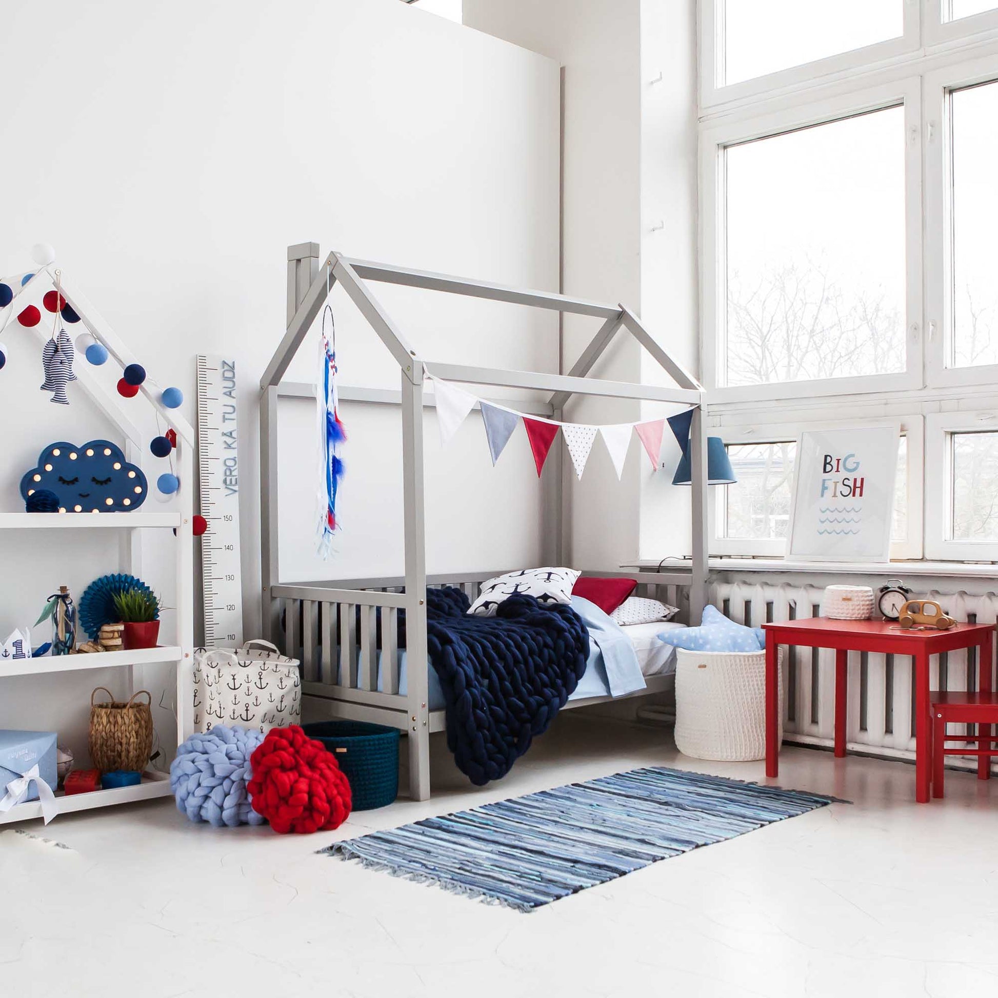 A child's room with a Raised house bed on legs with 3-sided rails, toys, and a bedside table.