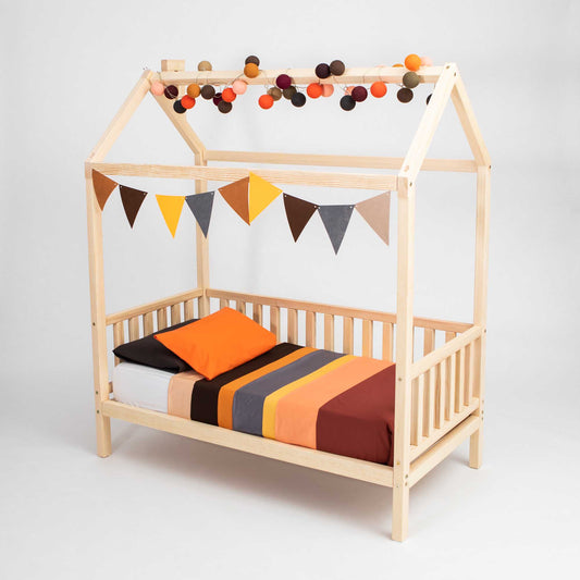 A raised house bed on legs with 3-sided rails, with bunting and pom poms.