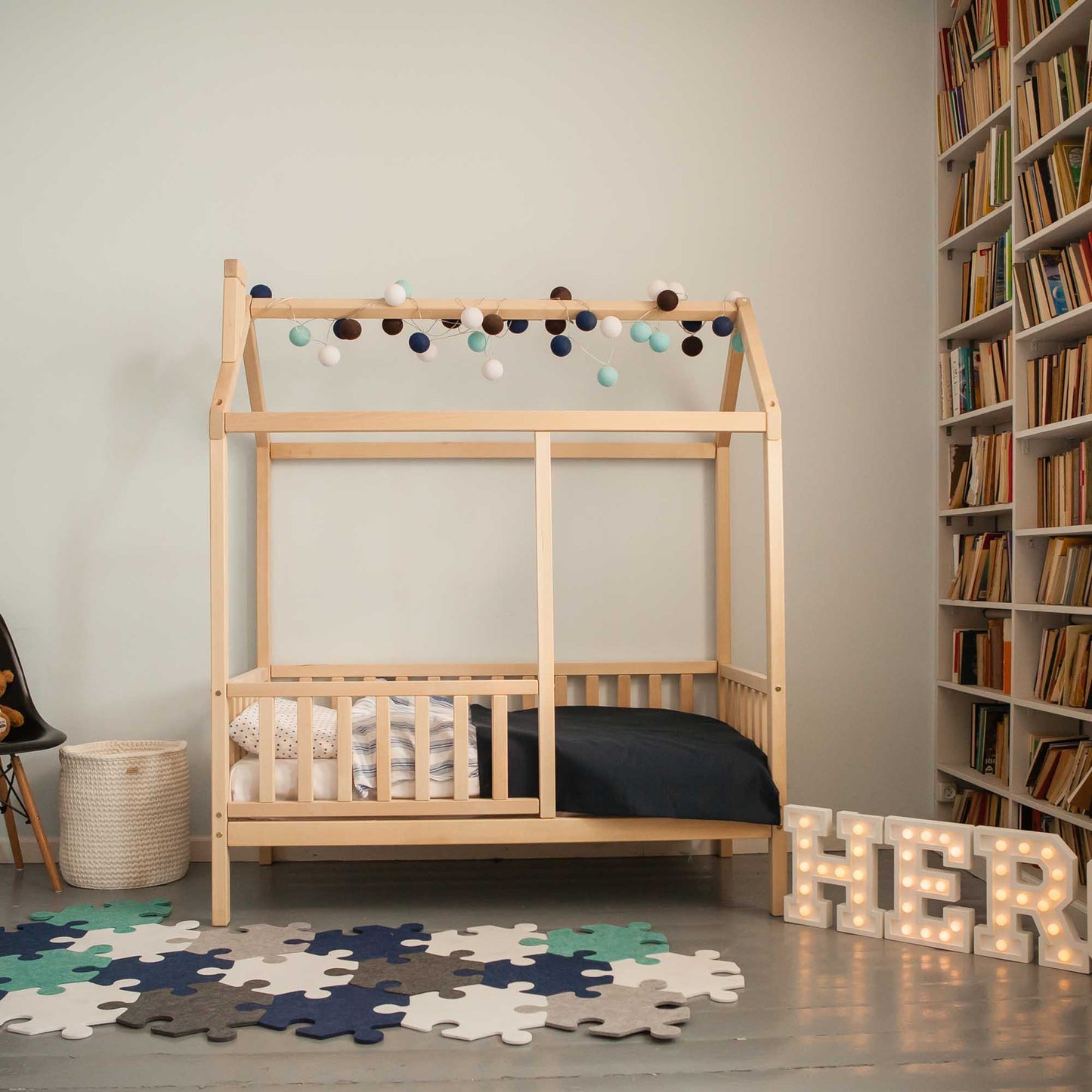A toddler's bedroom with a kids' house bed on legs with a fence and bookshelves.