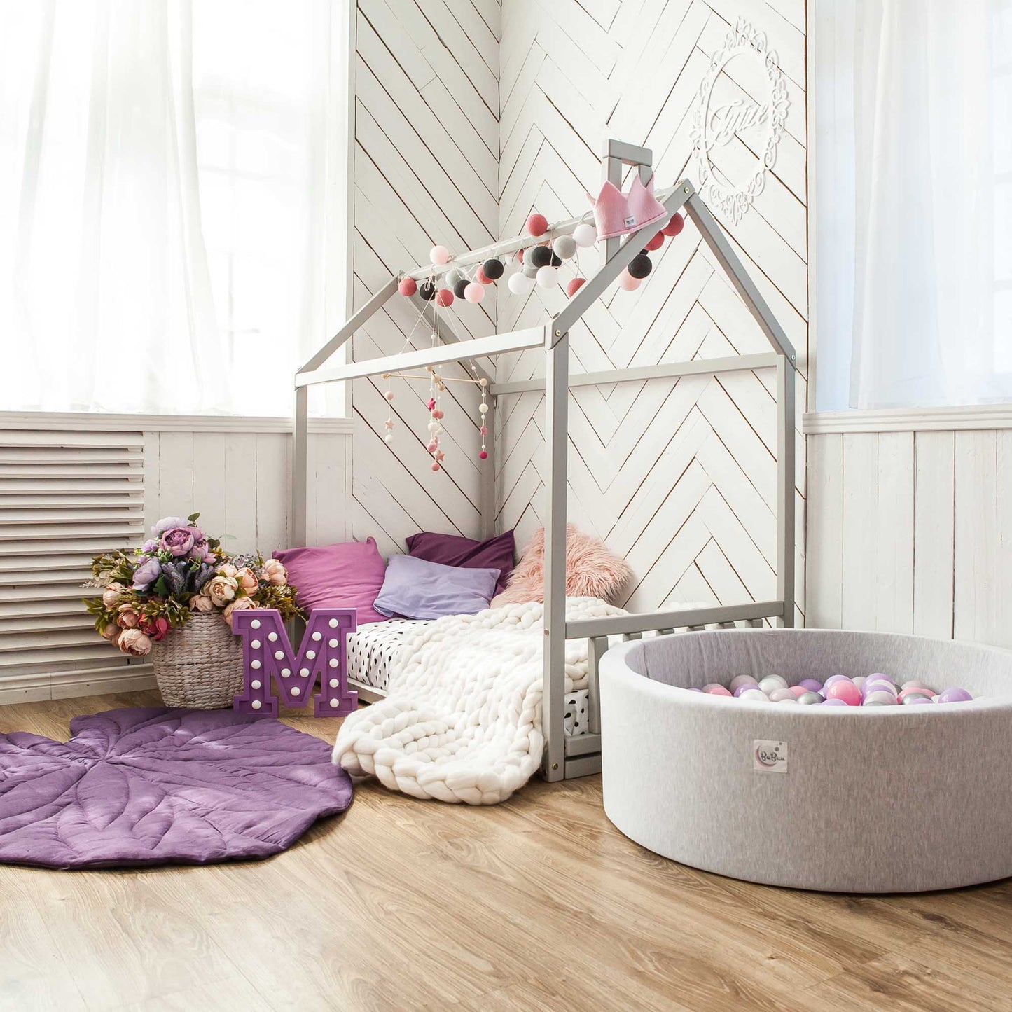 A cozy sleep haven, designed with the Montessori approach and featuring a Sweet Home From Wood toddler house bed with a headboard and footboard and a playful ball pit.