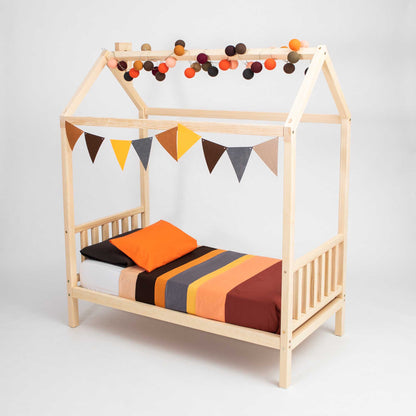 A Toddler house bed on legs with a headboard and footboard with bunting and pom poms.