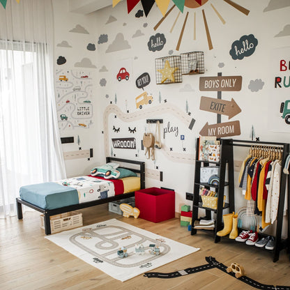 A children's bedroom with a transportation theme featuring wall decals of cars and roads, a kids' bed on legs with a horizontal rail headboard made of solid pine wood, an open wardrobe, toys, and colorful decorations. The room showcases a playful, organized setup.