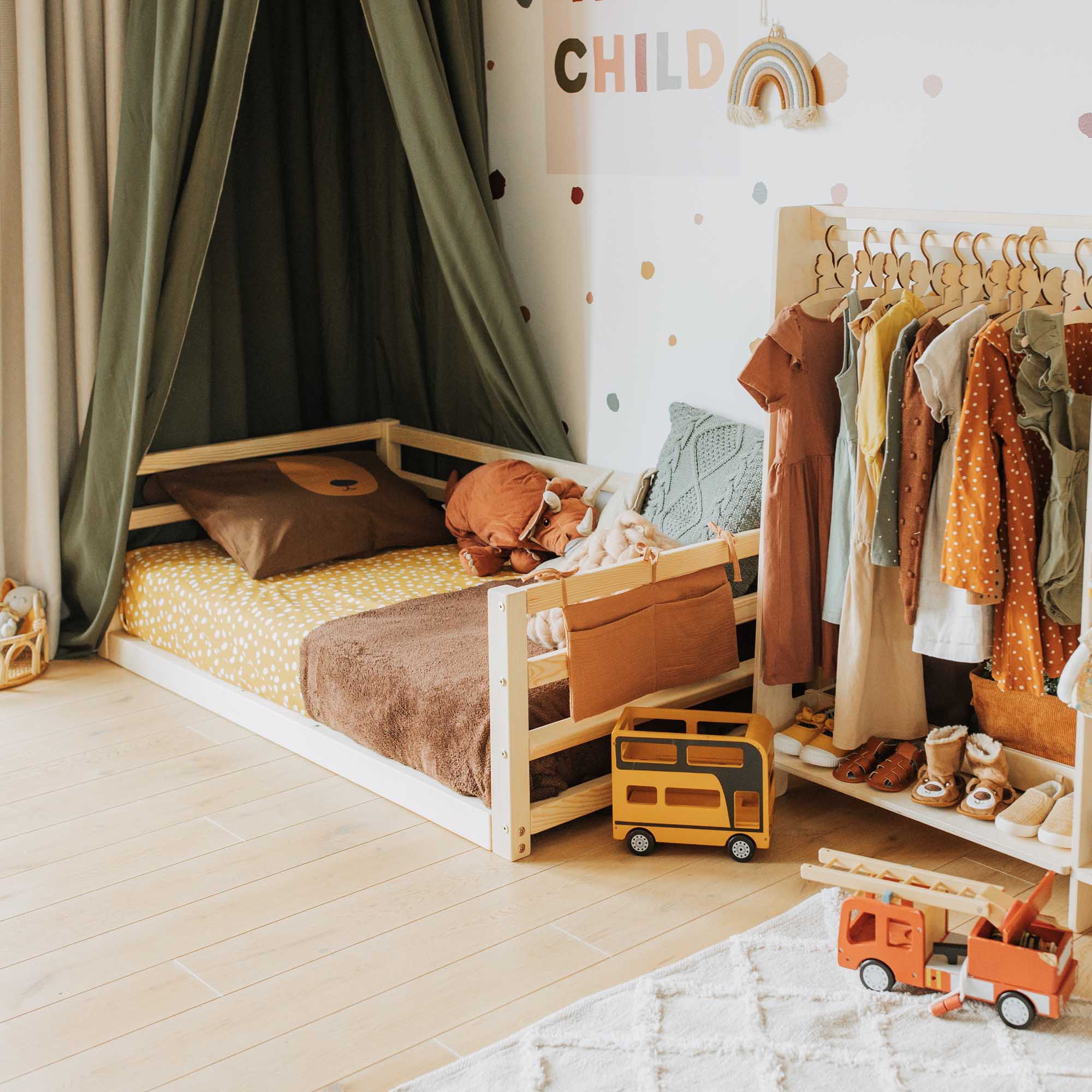 A child's room with a bed, clothes and toys.