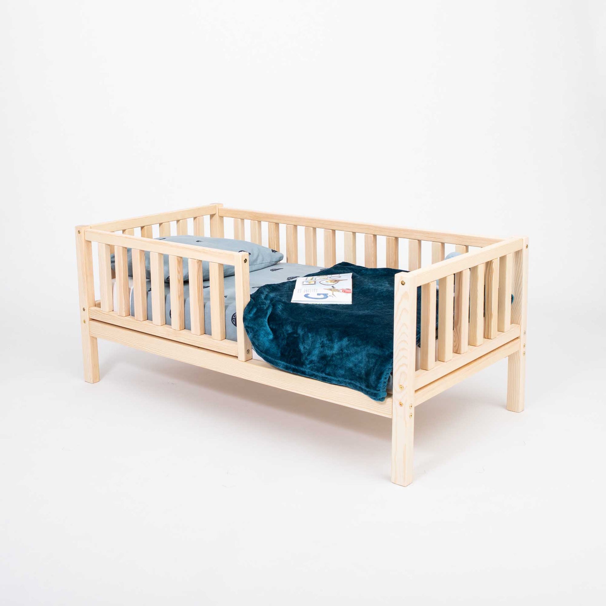 A Sweet Home From Wood 2-in-1 toddler bed on legs with a vertical rail fence, featuring a blue blanket.