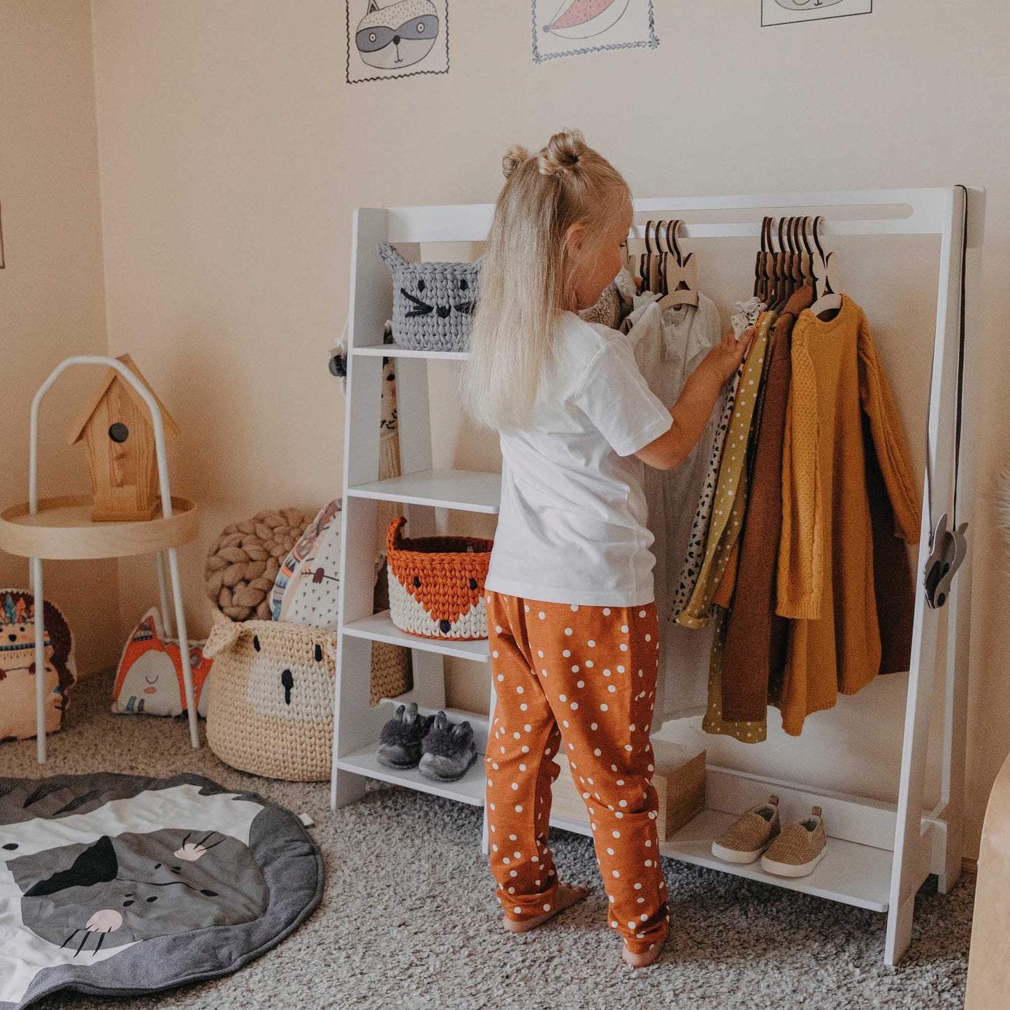A little girl standing next to an open Sweet Home From Wood children's wardrobe in a child's room.