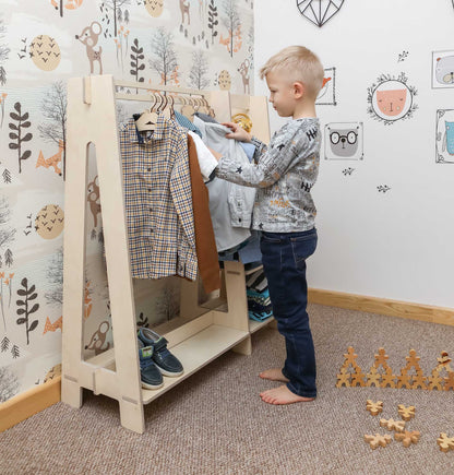 A young boy standing in front of a Sweet Home From Wood children's wardrobe, dress up clothing rack.