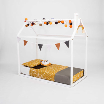 A cozy sleep haven for a child, adorned with bunting and pom poms, the Wooden zero-clearance house bed from Sweet Home From Wood.