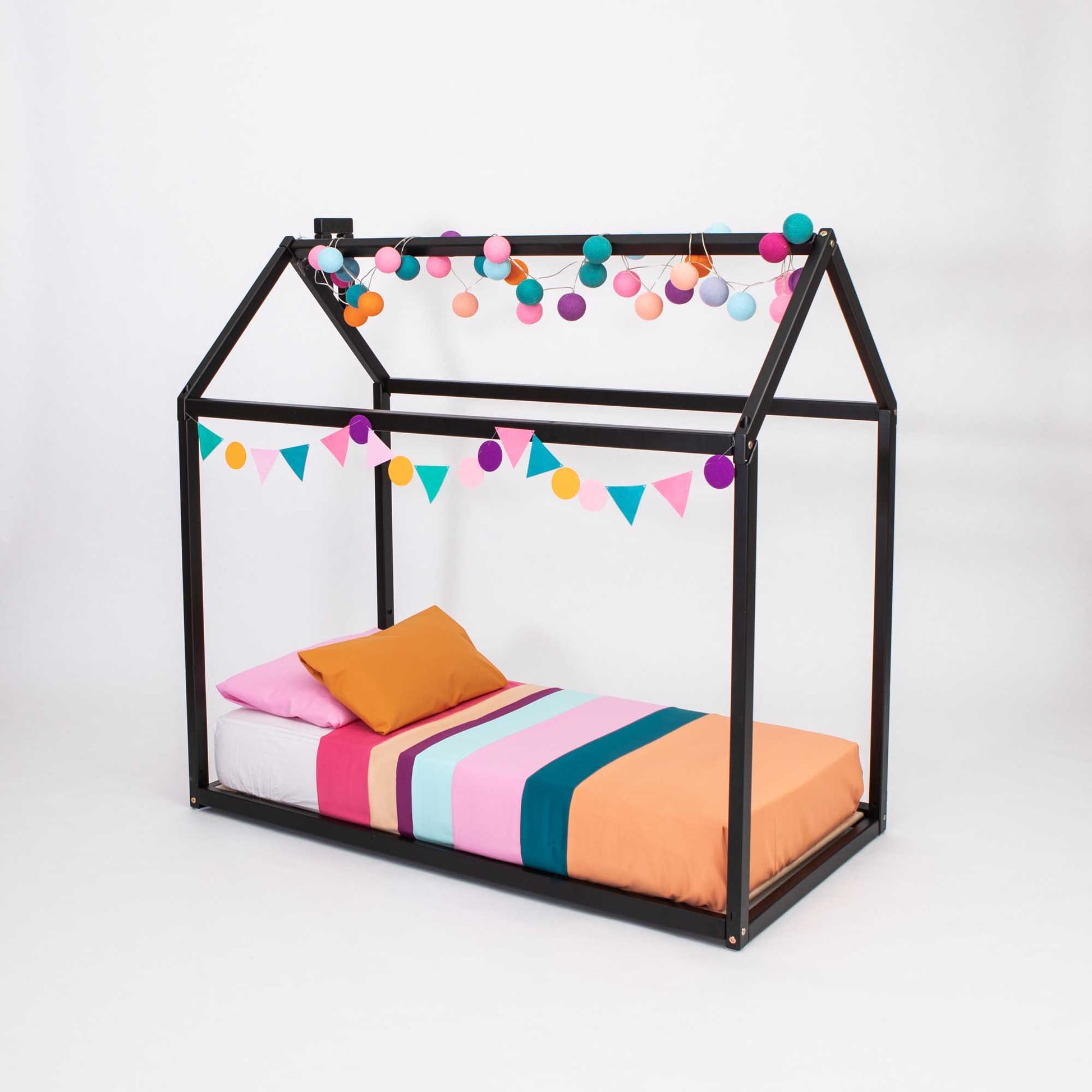 A Sweet Home From Wood Wooden zero-clearance house bed with a house-shaped canopy, providing a cozy sleep haven with colorful pom poms hanging from it.