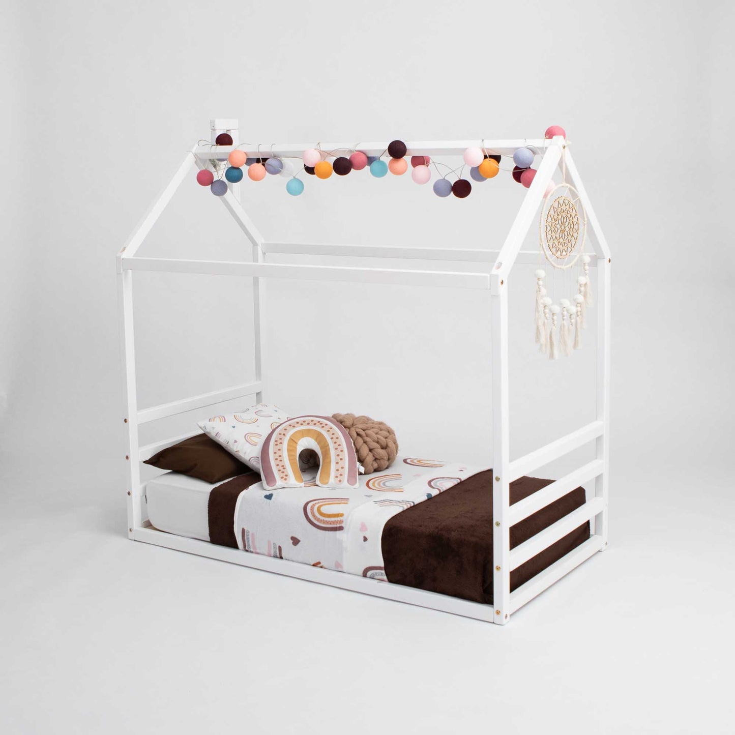A low platform bed with a wooden frame and pom poms, perfect as a Floor house-frame bed with a horizontal headboard and footboard for toddlers.