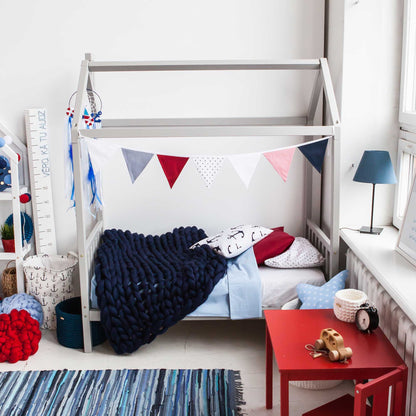 A child's bedroom with a toddler house bed on legs with a headboard and footboard and a rug.
