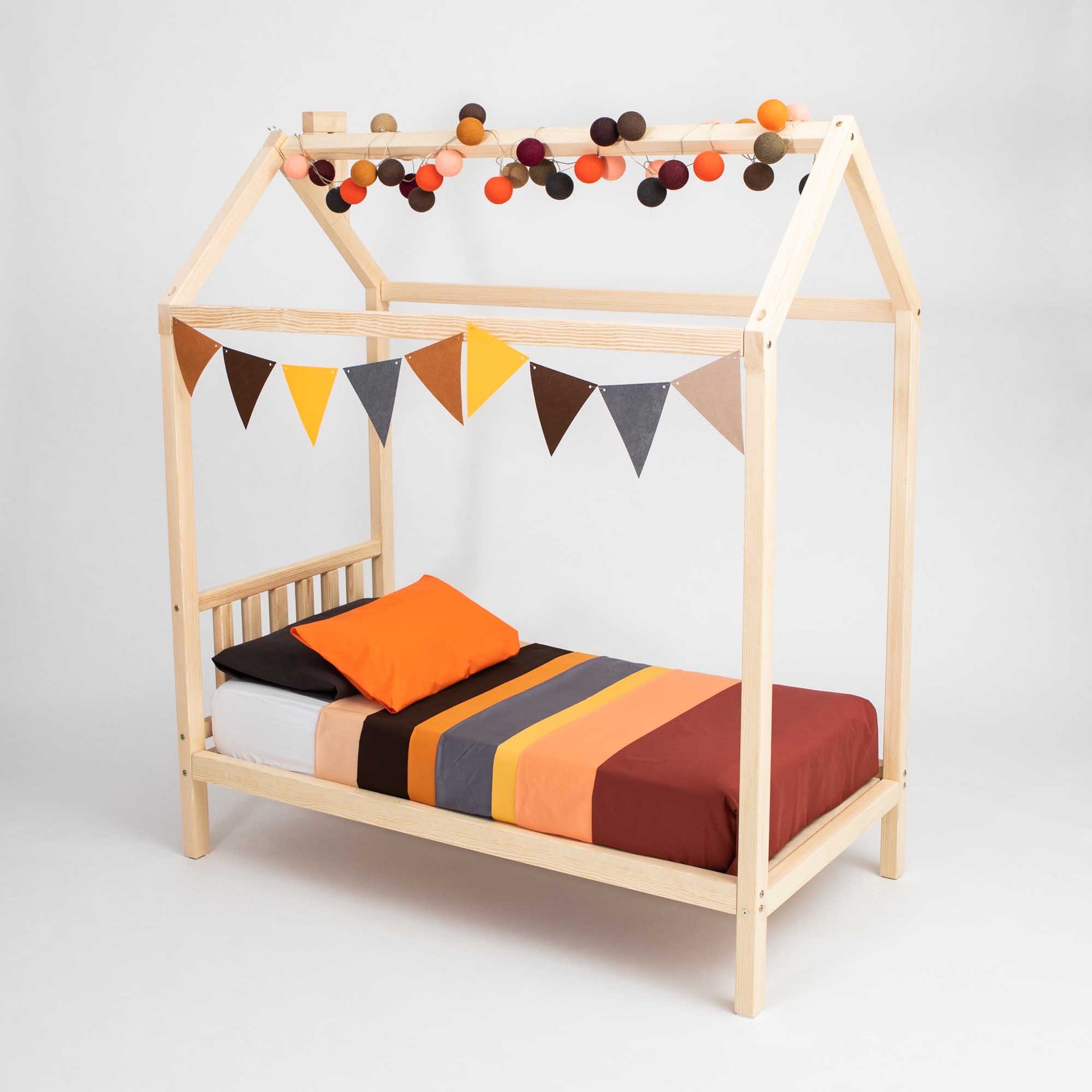 A TODDLERS' HOUSE BED ON LEGS WITH A HEADBOARD with bunting and pom poms.