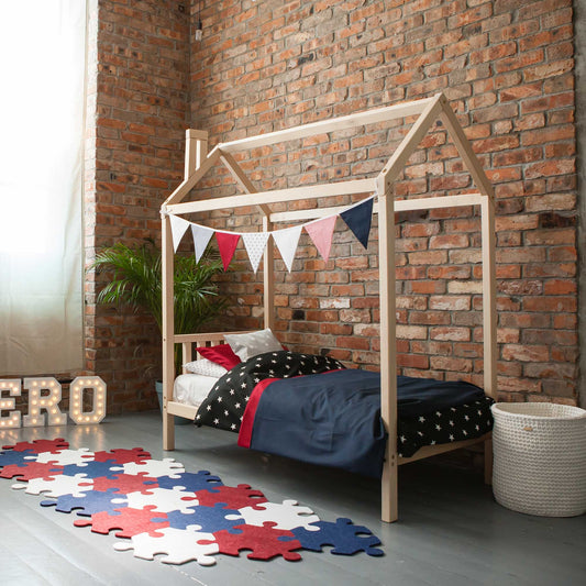 A Toddlers' house bed on legs with a headboard made of wood in a room with brick walls.