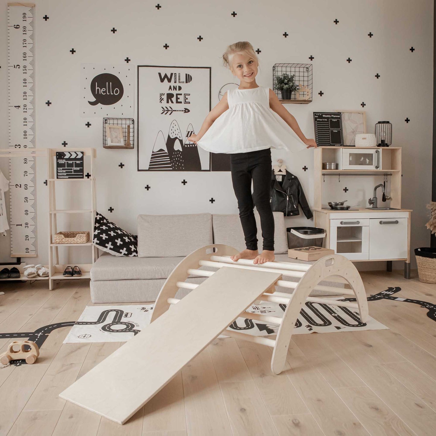 A little girl standing on a Climbing arch, Foldable climbing triangle, and a ramp in a child's room.