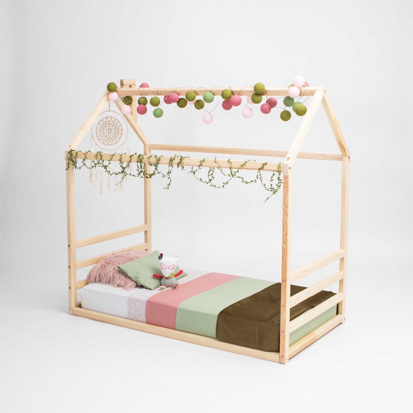 A Sweet Home From Wood floor house-frame bed with a horizontal headboard and footboard, featuring pom poms, creating a cozy sleep haven for little ones.