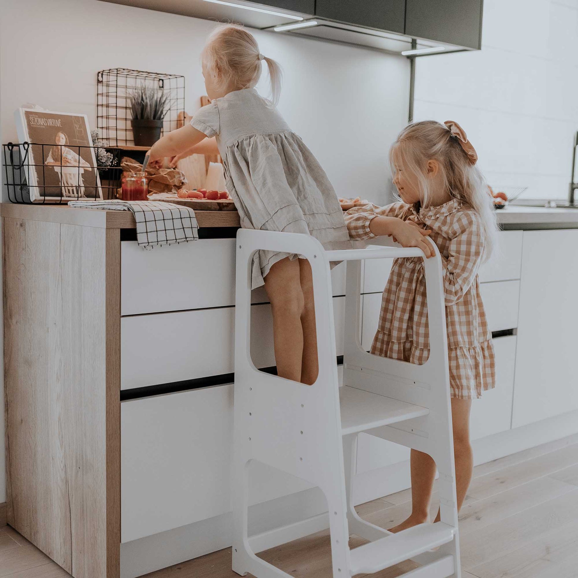 Two little girls standing on a Sweet Home From Wood Kids' kitchen tower with 3 height levels in a kitchen.