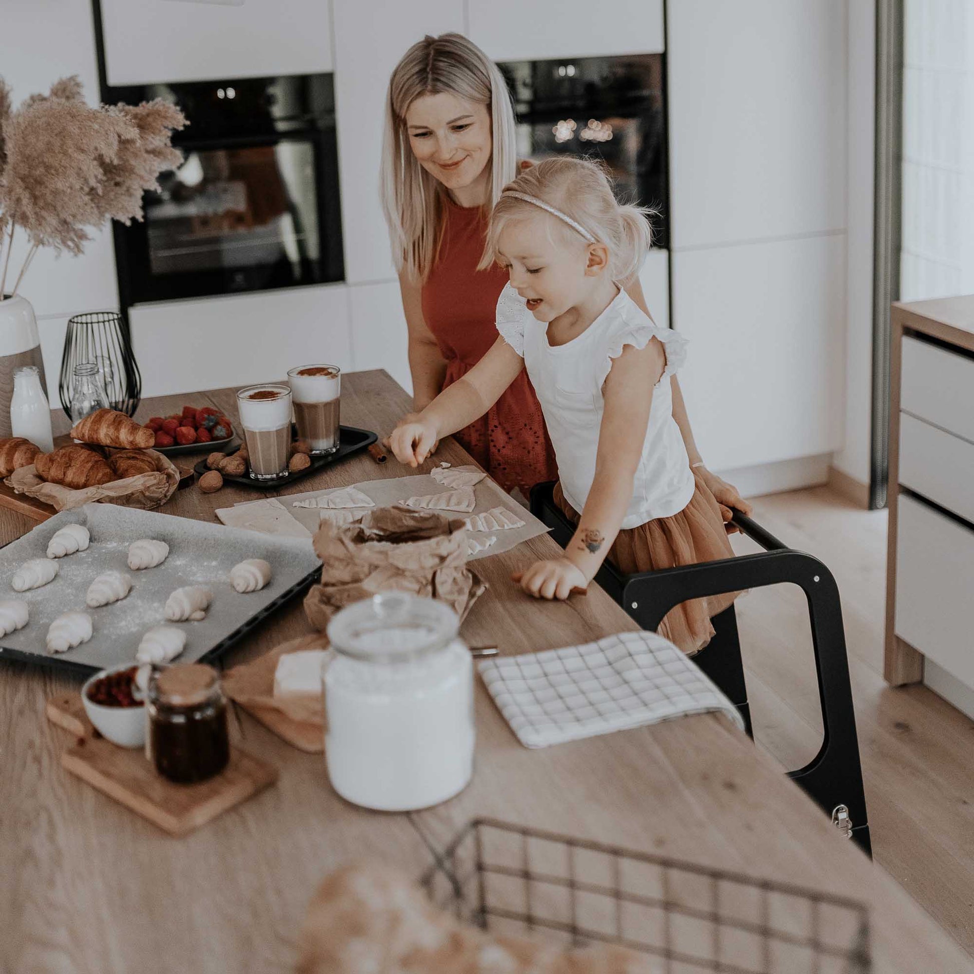 A mother and daughter using a Sweet Home From Wood Kids' kitchen tower with 3 height levels in the kitchen to make breakfast.