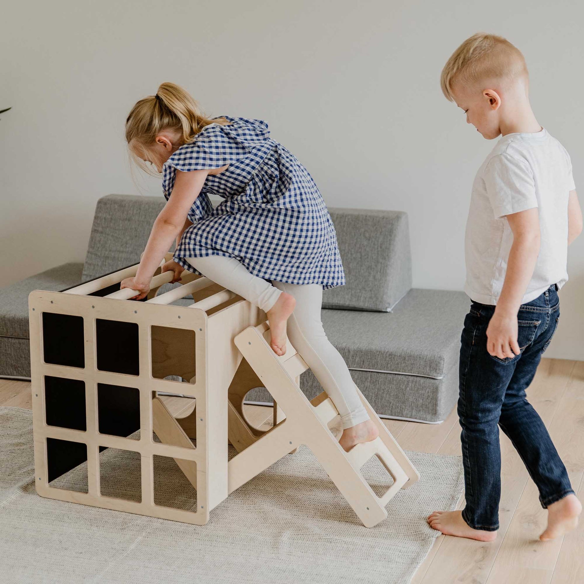 Two children play with a Sweet Home From Wood climbing arch + transformable climbing cube / table and chair  + a ramp in a living room.