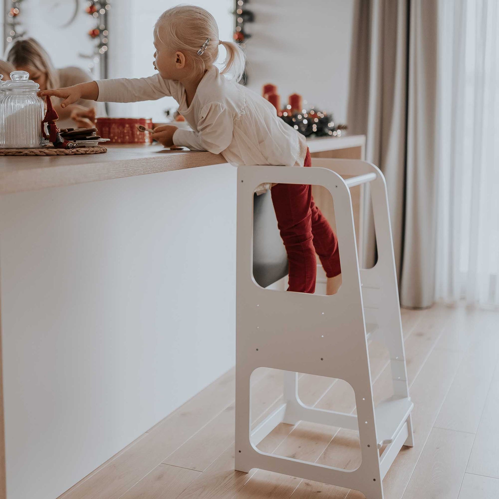 A little girl standing on a white step stool in a Sweet Home From Wood kitchen tower with blackboard for kids.