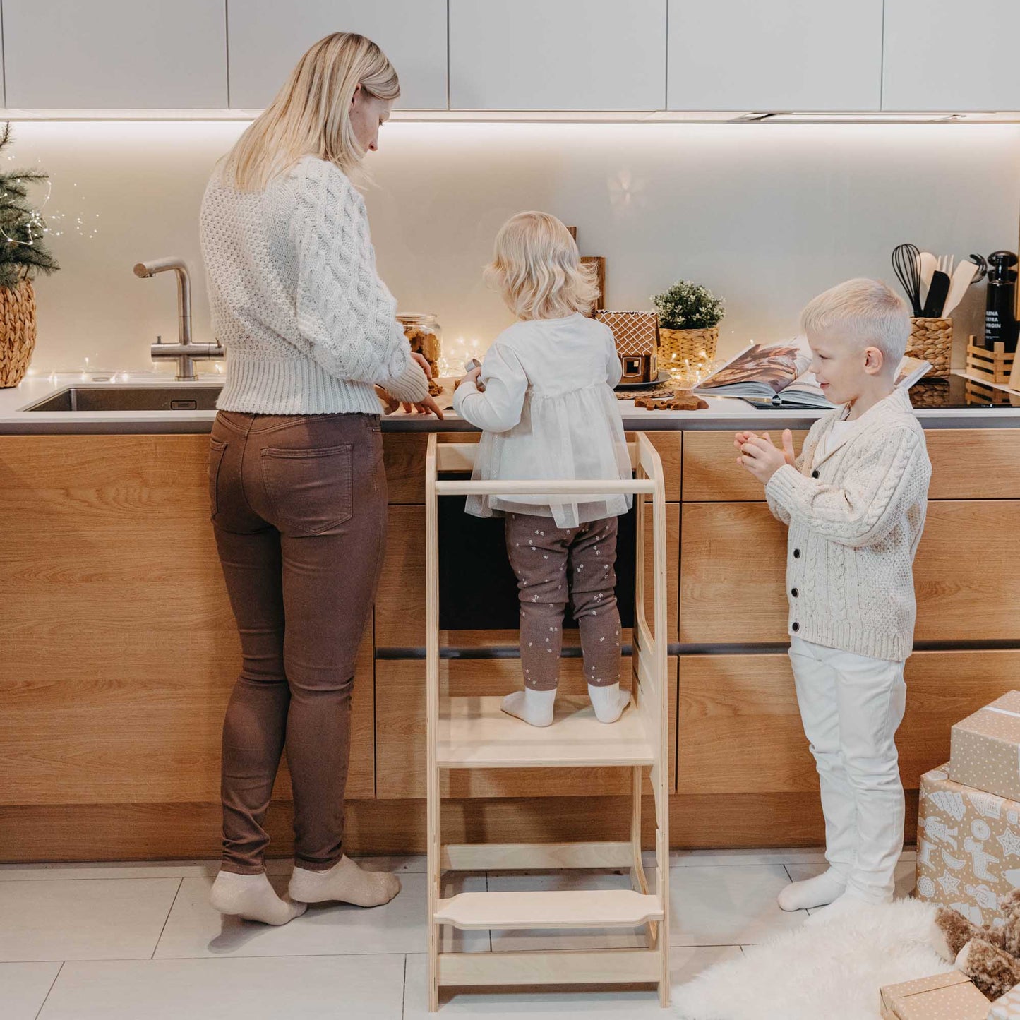 A woman and two children using a Sweet Home From Wood kitchen tower with blackboard in a kitchen.