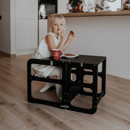 A little girl sitting at a table with a 2-in-1 transformable kitchen tower - table and chair set.