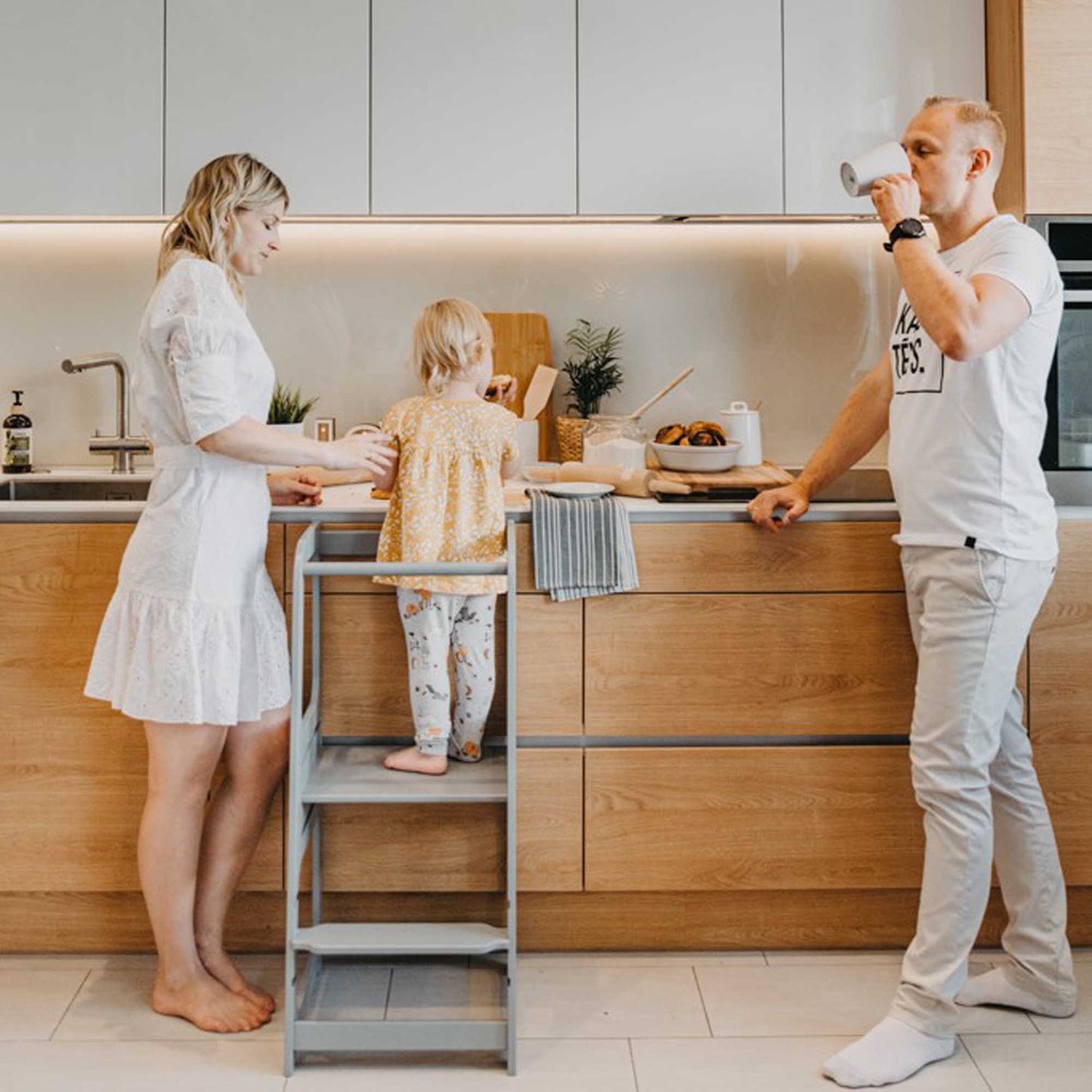 A family using the Kids' Kitchen Tower with 3 height levels from Sweet Home From Wood in a kitchen.