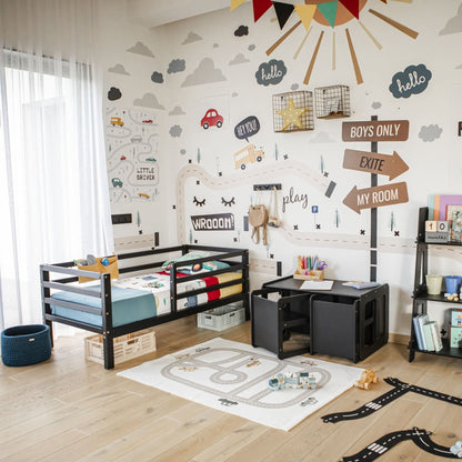 A child's room with a Kids' bed on legs featuring a horizontal rail fence, solid pine or birch wood shelves holding books and toys, wall decorations including streets and signs, a small table with chairs, and a play mat shaped like a street.