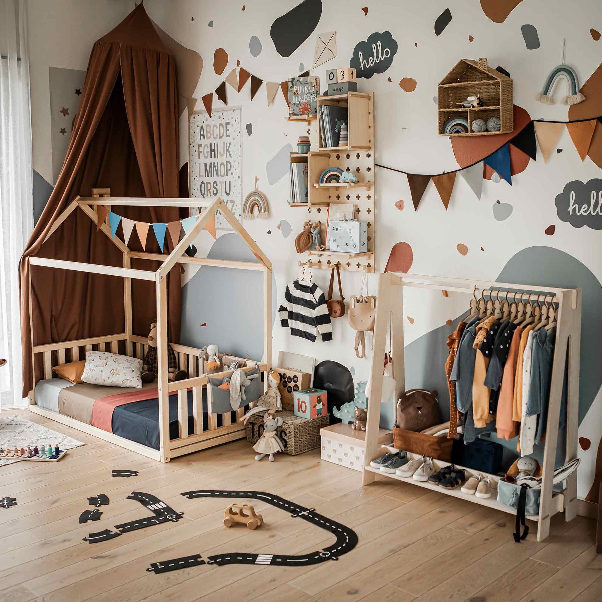 A kids' bedroom featuring a wooden house-frame bed, an area designated for play, a Kids' clothing rack for dress-up storage, toys scattered around, and wall shelves adorned with various decorations. The room is decorated in a beige and brown color scheme.