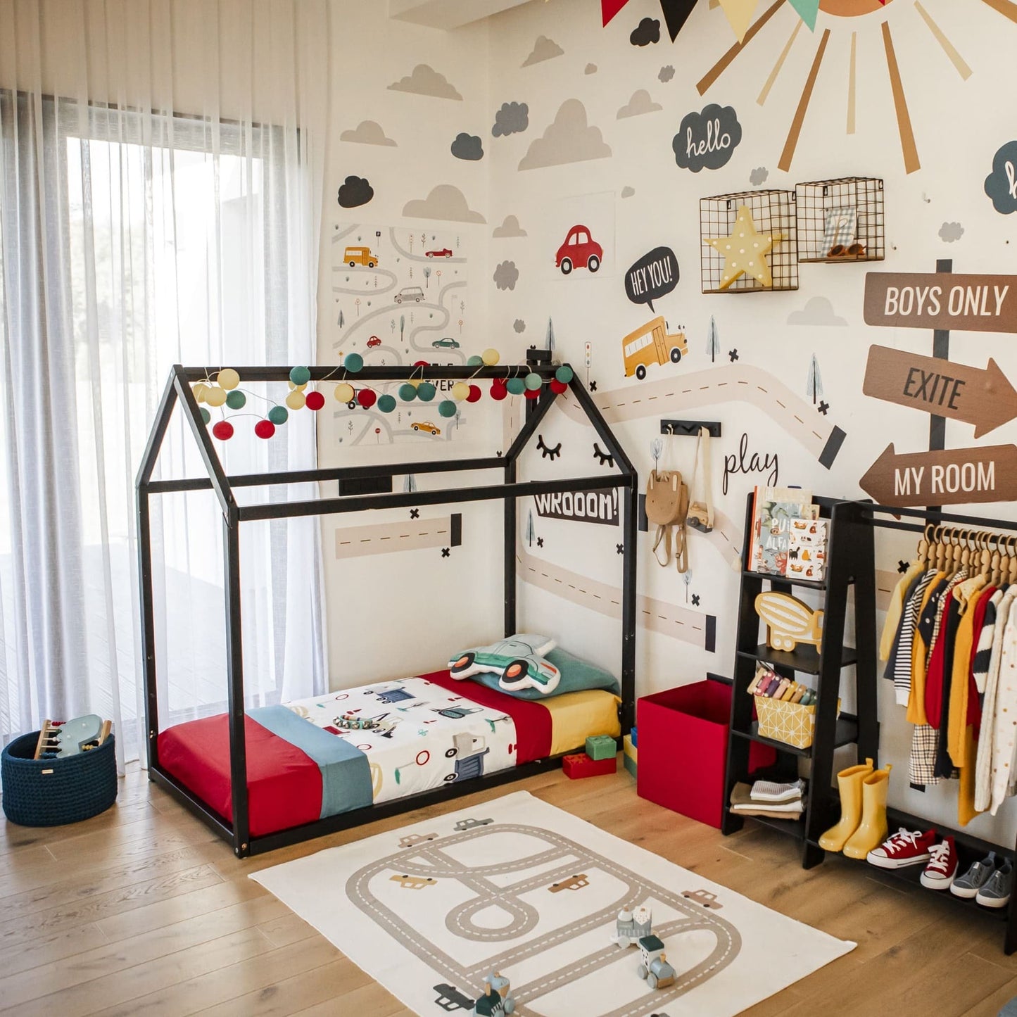 A children's bedroom featuring a Wooden zero-clearance house bed, vibrant decorations, wall stickers, a clothes shelf, and a play mat on the floor. The room exudes a bright and playful atmosphere.