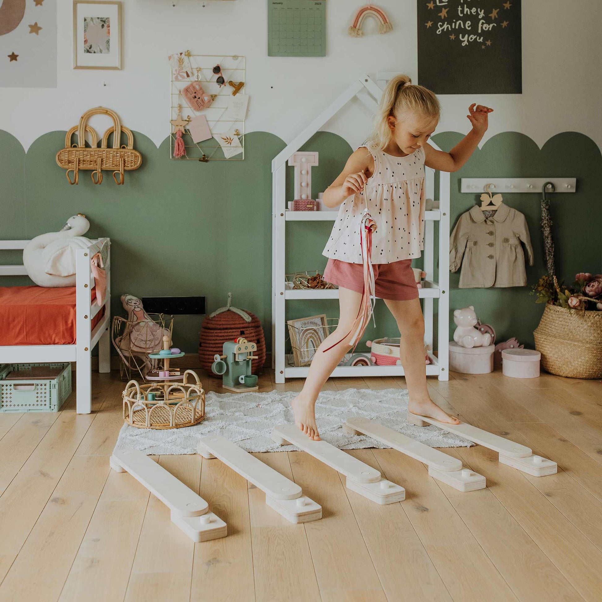 A young girl hones her motor skills by balancing on the Balance Beam Set in a well-decorated, colorful room filled with toys and children's furniture.