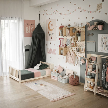 A well-organized children's room featuring a Kids' bed with a headboard and footboard, complemented by a canopy, wall decorations, storage bins, toys, and clothes racks. The decor includes pastel colors and a "Dream Big" sign. Light wood flooring brightens the space.