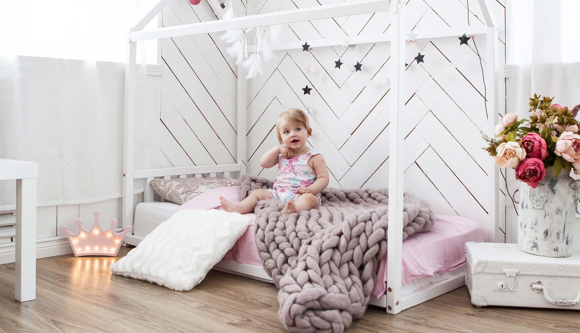 A little girl is sitting on a bed in a pink and white room.