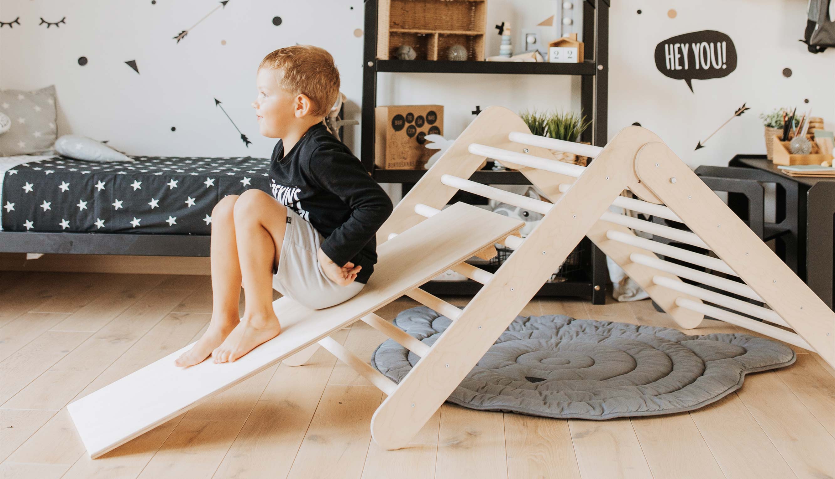 A boy is sitting on a wooden slide in his room.