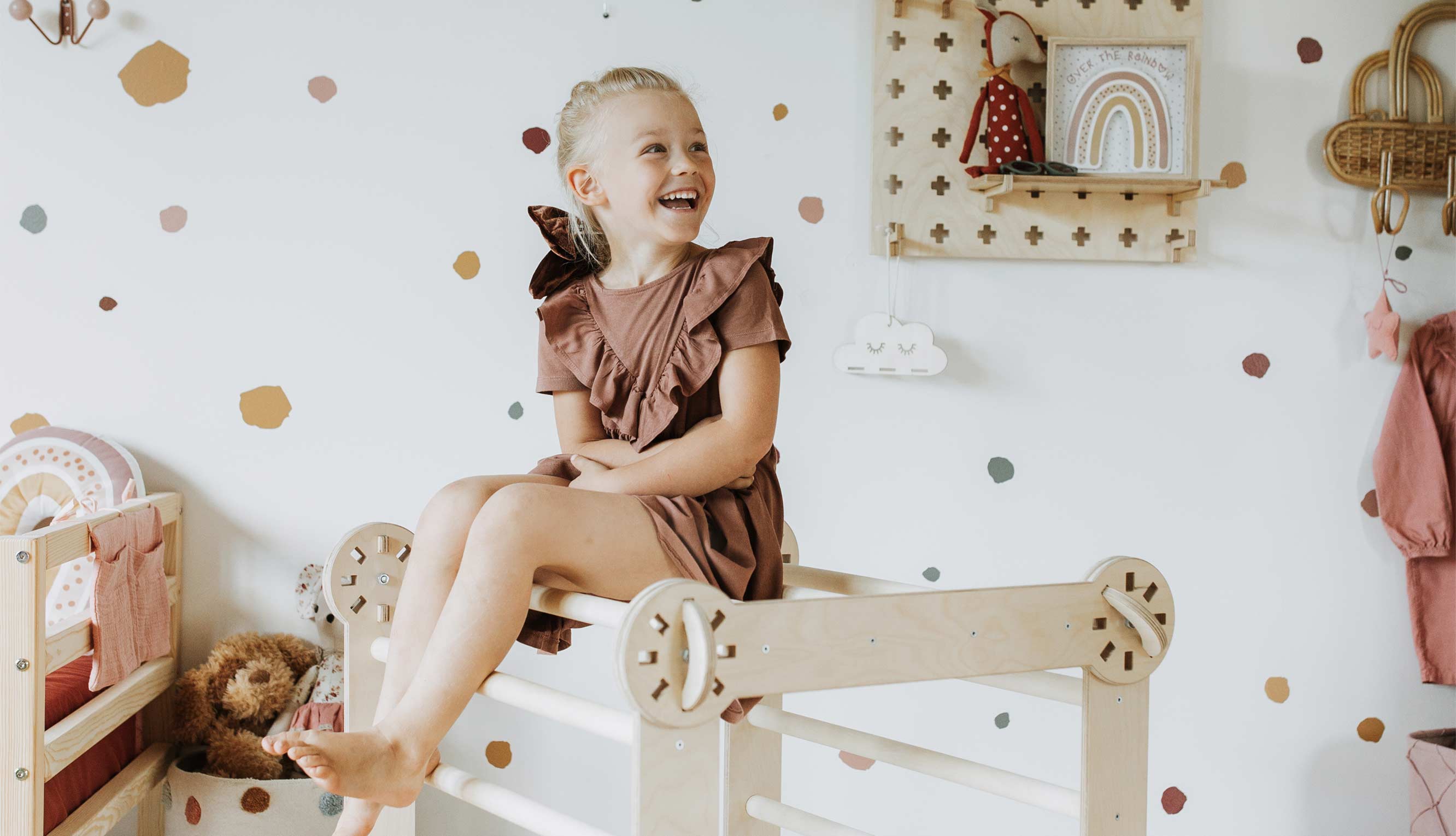 A little girl sitting on a wooden bunk bed in her room.