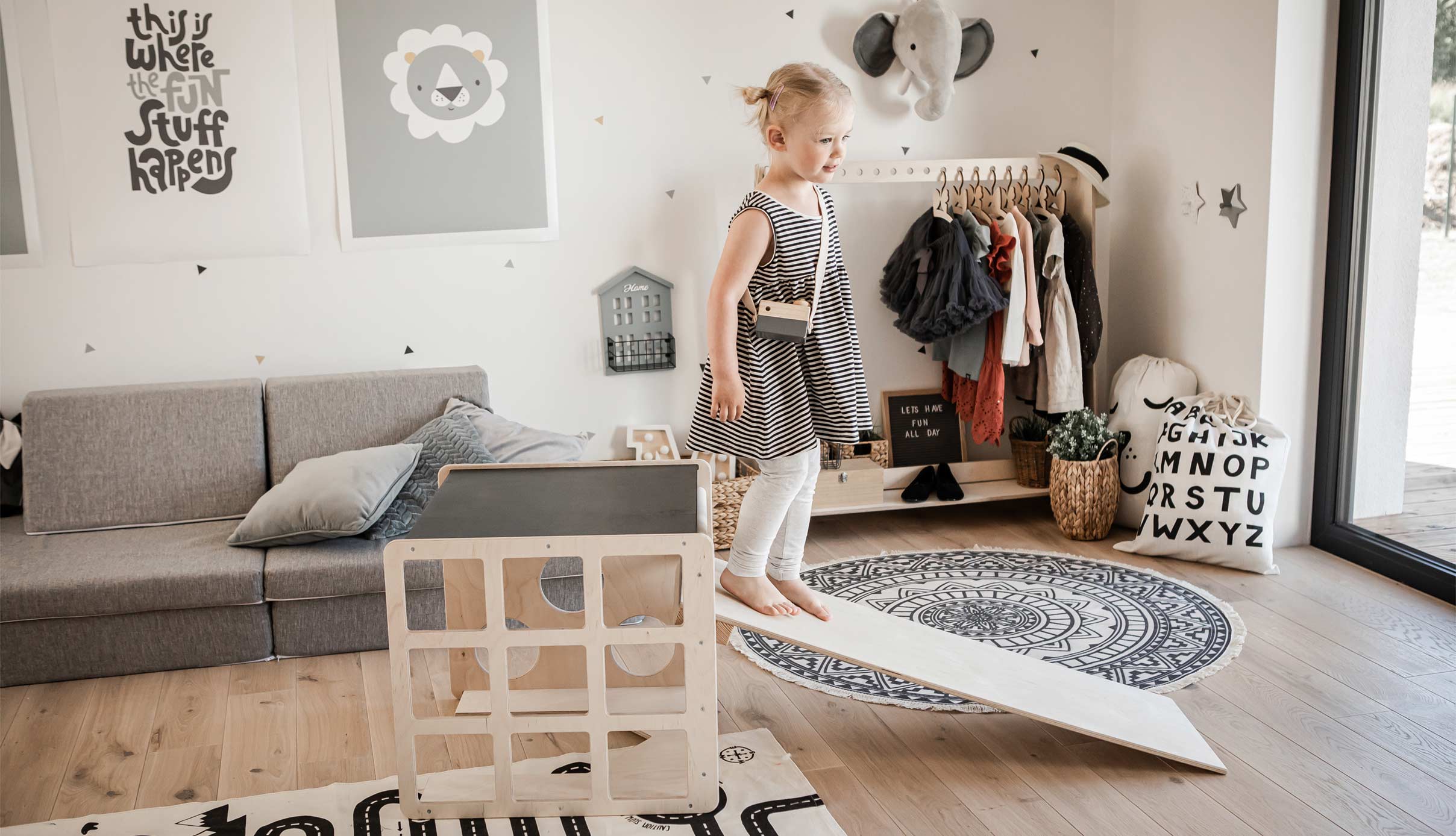 A little girl standing on a wooden platform in a living room.