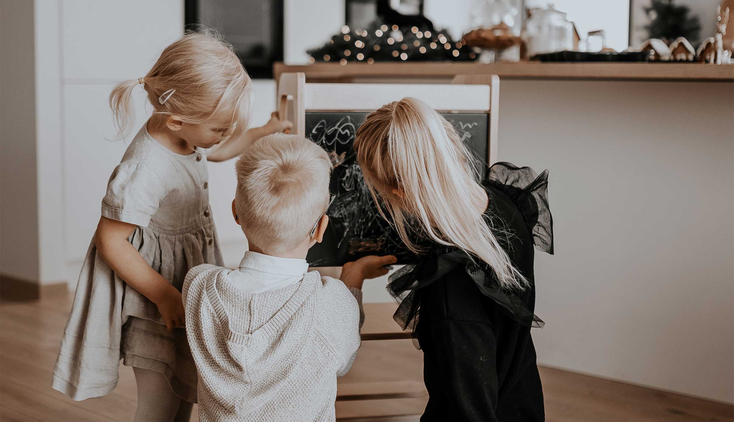 Three children drawing on a chalkboard in a living room.