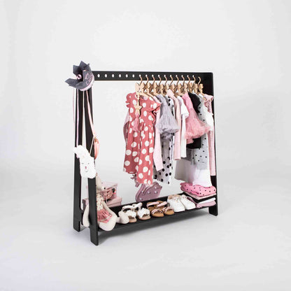 The Montessori clothing rack serves as a compact wardrobe, displaying a variety of garments and accessories, including dresses, shoes, hats, and socks, all neatly organized on hangers and shelves.