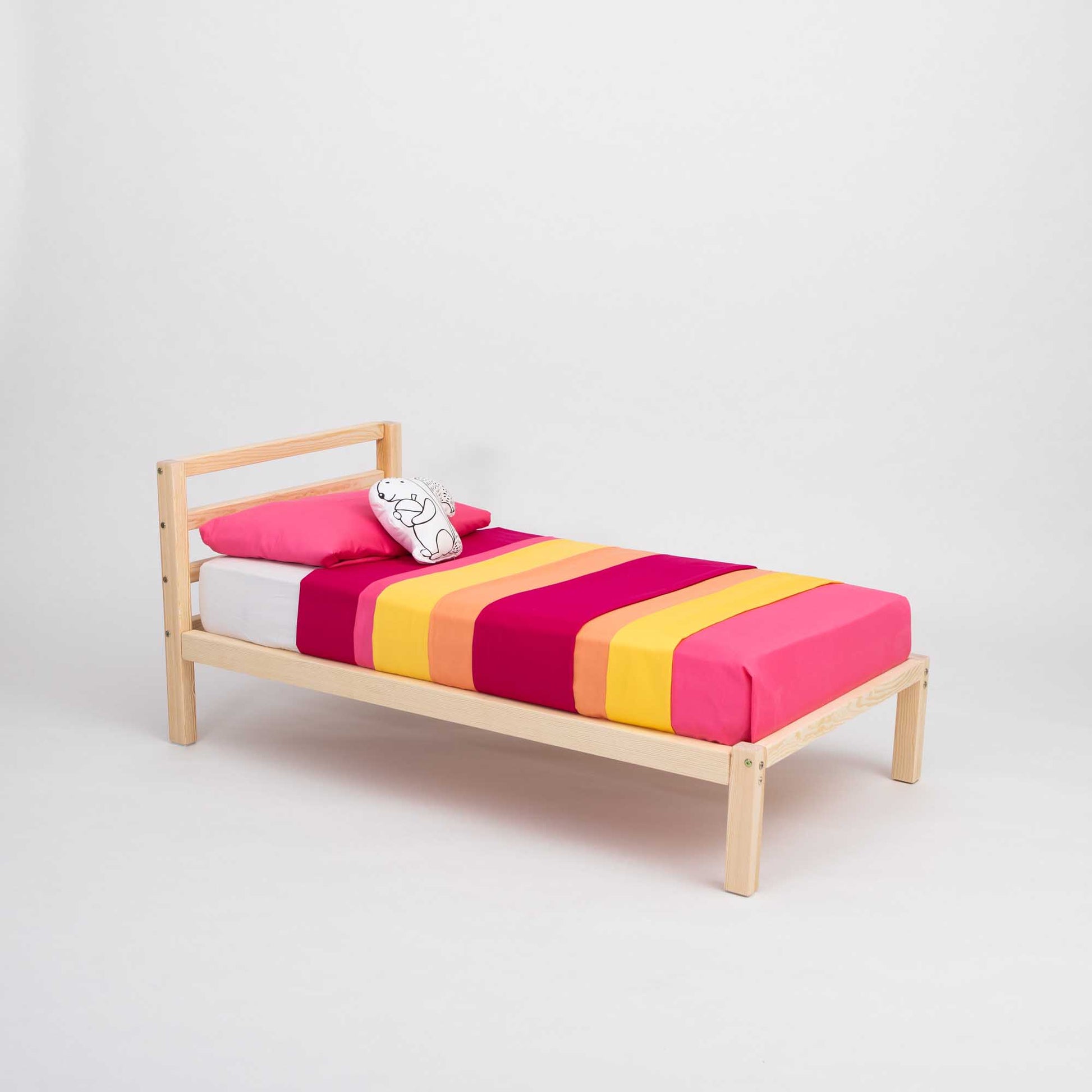 A Kids' bed on legs with a horizontal rail headboard from Sweet Home From Wood, with a pink and yellow striped blanket.