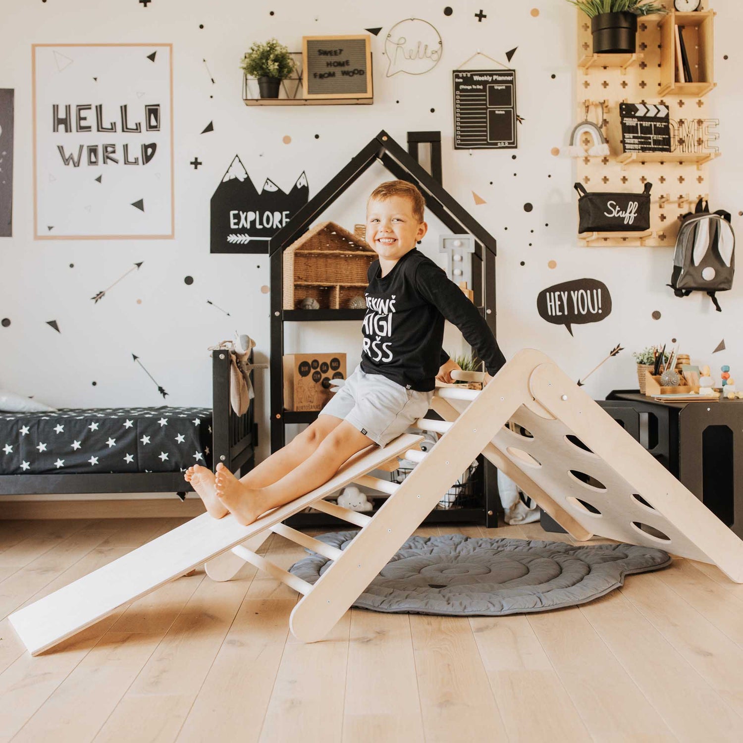 A boy sitting on a Sweet Home From Wood Climbing arch + Transformable climbing triangle + a ramp in a playroom.