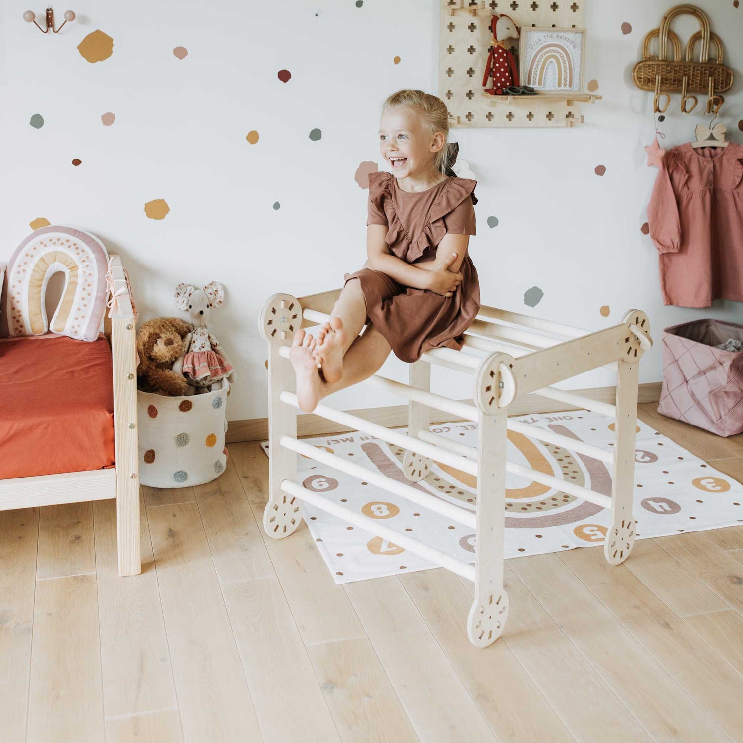 A little girl sitting on a wooden chair in a Transformable climbing gym.