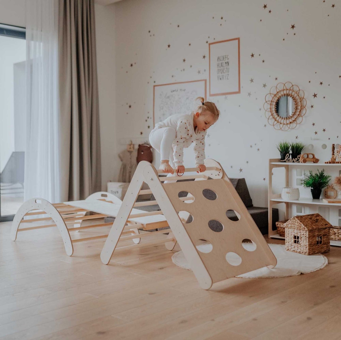 A child is standing on the Sweet Home From Wood Climbing arch + Transformable climbing triangle + a ramp in a room.