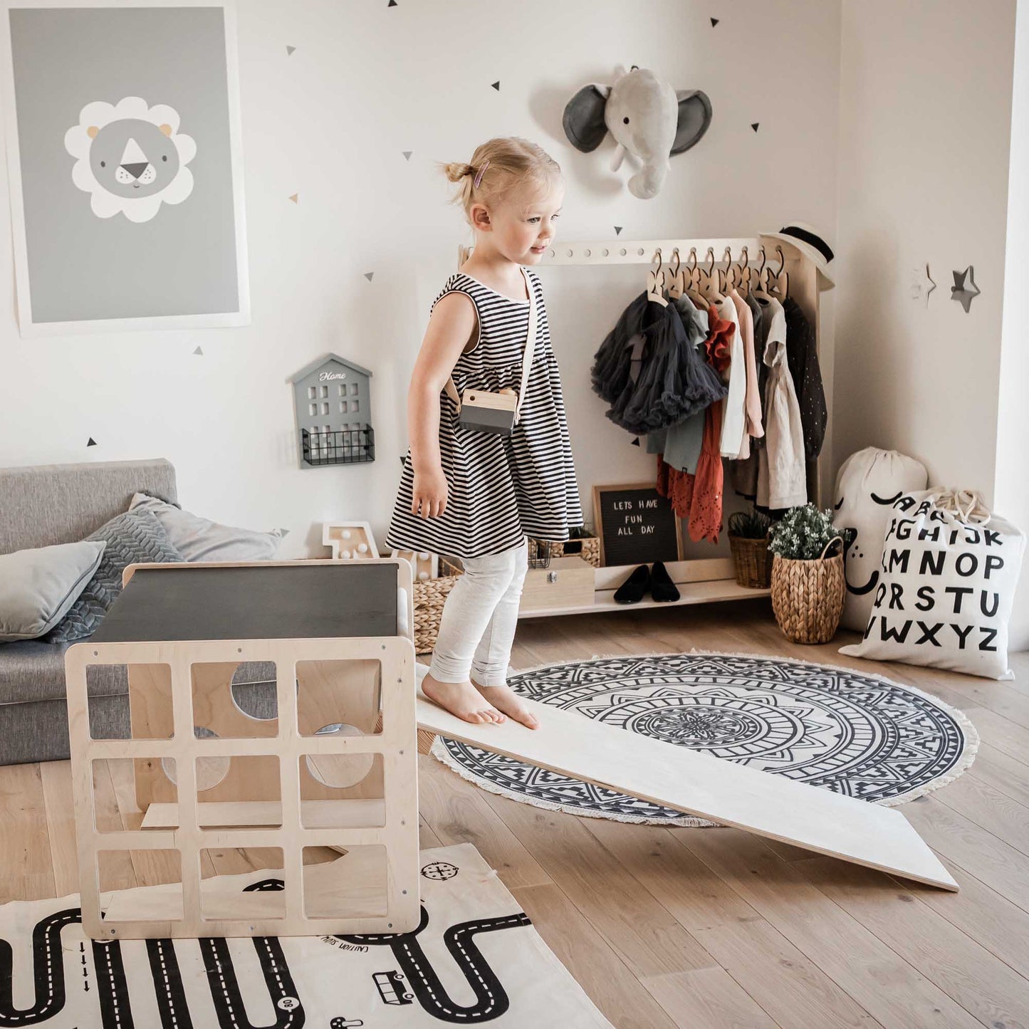 A little girl standing on a Transformable climbing cube / table and chair + ramp in a playroom.