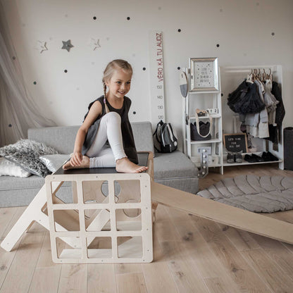 A little girl sitting on a Transformable climbing cube / table and chair + ramp in a living room.