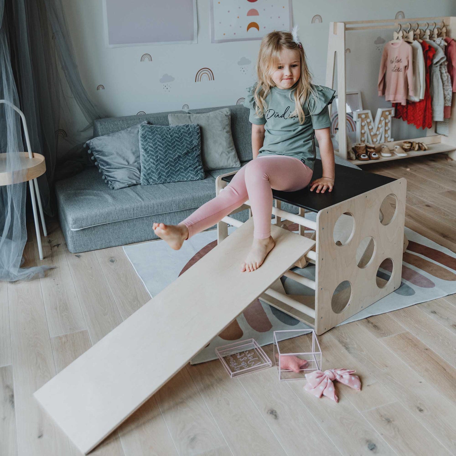 A little girl sitting on an Activity cube with sensory panels and a ramp from Sweet Home From Wood in a room.
